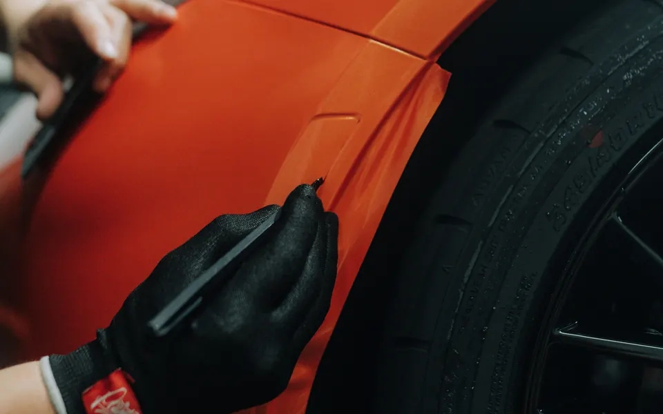 Orangefarbene Folie wird mit Handschuh und Rakel an einen Kotflügel angelegt