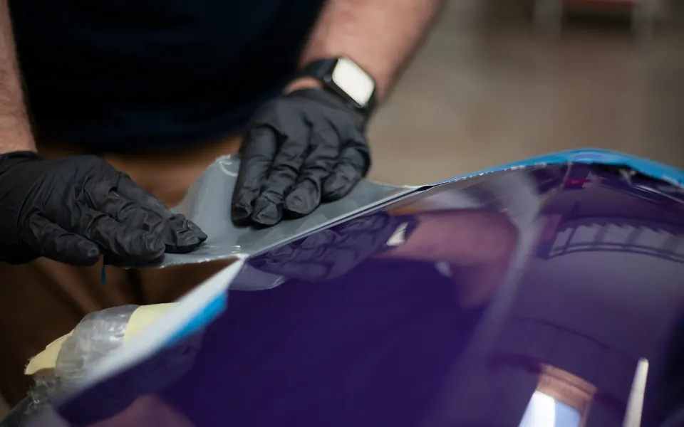Lackschutzfolie wird mit beiden Händen auf eine blaue Motorhaube gelegt